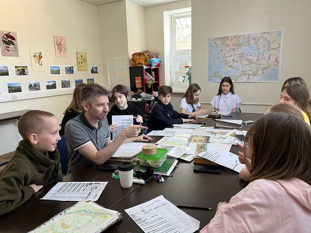 Педагог сидит за одним столом с группой детей, перед ними карты и рабочие листы